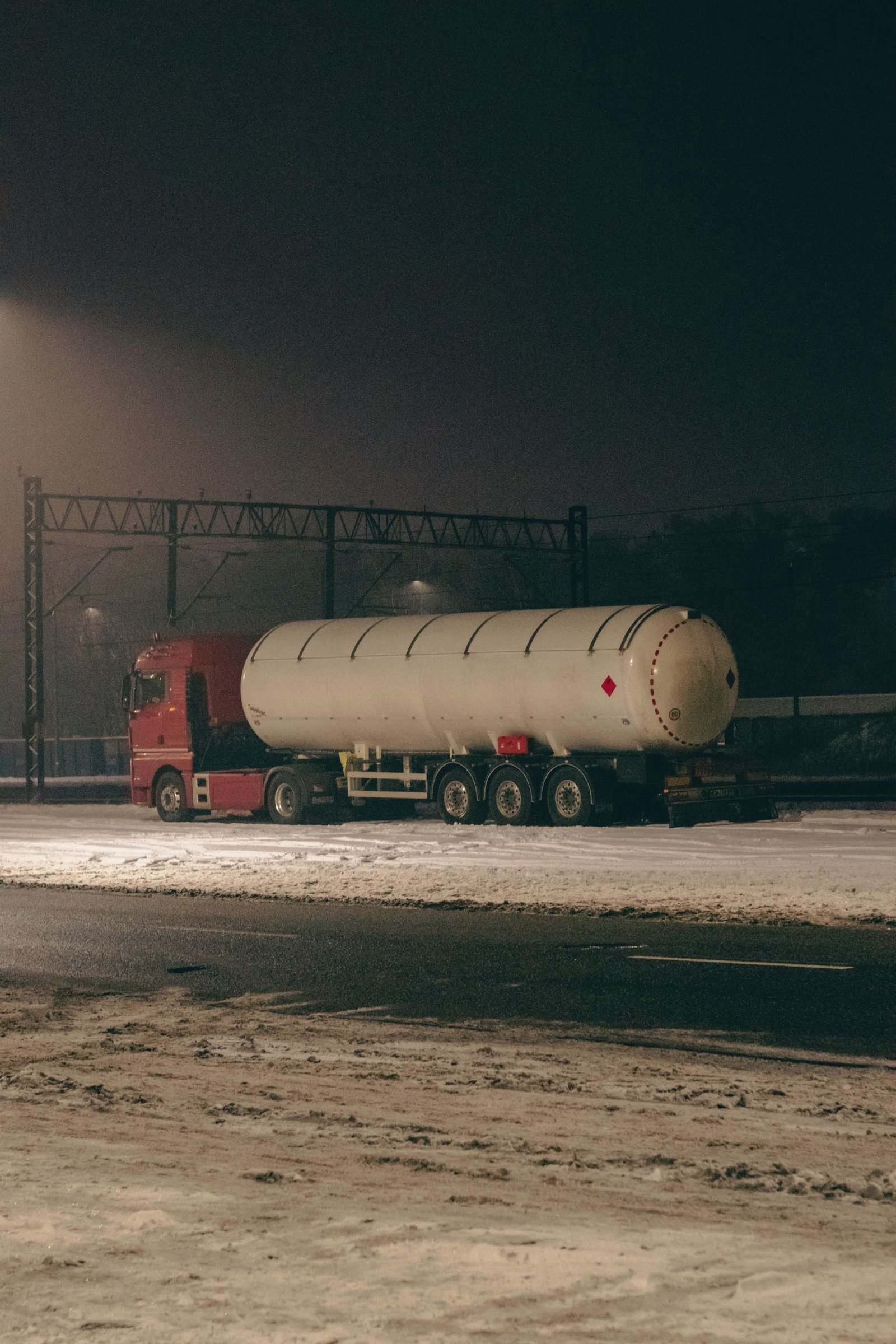 A gas tank trailer parked at night on a snowy lot under floodlights