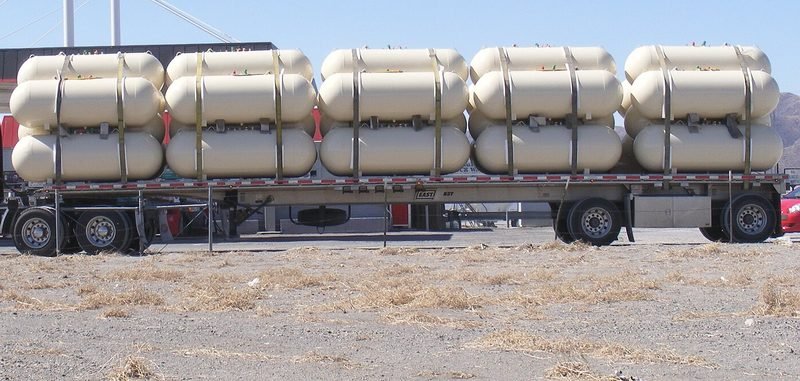 Stacks of new horizontal propane tanks strapped onto a flatbed trailer